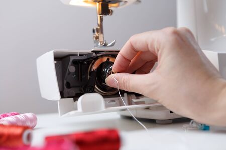 Girl inserts bobbin in sewing machine placed on table