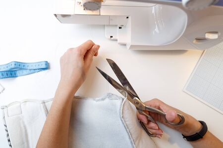 Woman on background of sewing machine cuts thread with scissors