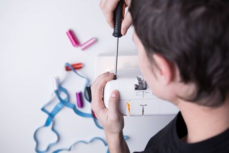 Man with screwdriver repairing sewing machine on empty gray background