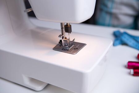 Sewing machine on table with coils of red thread and measuring tape