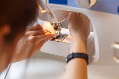 Girl sews fabric on machine sitting indoors