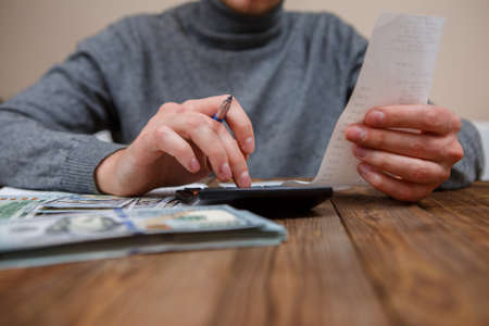 savings, finances, economy and home concept - close up of hands with calculator counting money and making notes at homeの写真素材