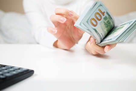 business, finance, saving, banking and people concept - close up of woman hands counting us dollar...