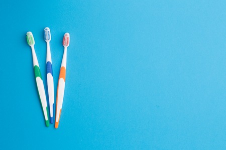 Three multi-colored toothbrushes on left at empty blue background, place for inscriptionの写真素材