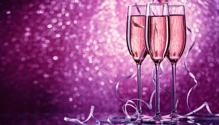 Picture of three wine glasses with sparkling champagne with white ribbons on pink backgroundの写真素材