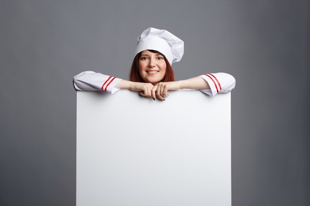 Photo of smiling brunette chef in white dressing-gown cap with empty paper in handsの写真素材