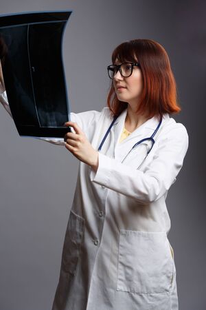 Image of female doctor in glasses and white robe with looking at x-ray on empty gray backgroundの写真素材