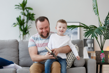 Photo of father and son reading book sitting on gray sofaの写真素材