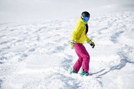 Image of female athlete wearing helmet and mask, snowboarding from snowy mountain slopeの写真素材