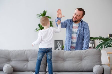 Family photo of young son standing on sofa making handshake with dadの写真素材