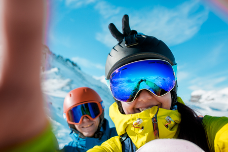 Photo of sports man and woman in helmet doing selfie on background of snowy hillsの写真素材