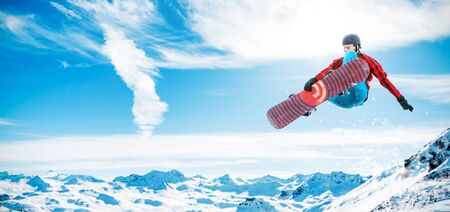 Panoramic photo of athlete jumping on snowboard at background of snowy mountainsの写真素材