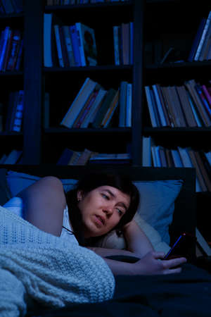 Portrait of woman with phone lying in bed at night