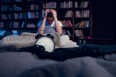 Photo of brunet with insomnia sitting in bed with alarm clockの写真素材