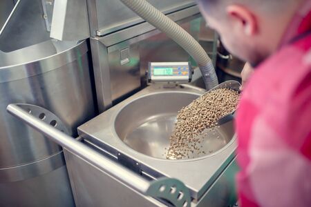 Photo of man with scoop with coffee beans at coffee grinder