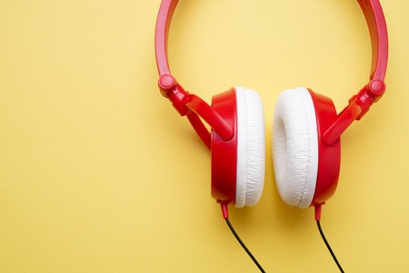 Image of red and white headphones for music close-up on empty yellow background with place for...