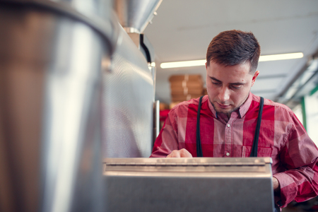 Photo of young man with phone at computer of industrial machineの写真素材