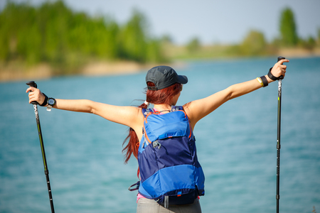 Picture of back of sporty woman with walking sticks and backpack on lake backgroundの写真素材