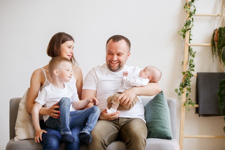 Photo of smiling parents with two young sons sitting on sofaの写真素材