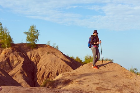 Photo of tourist woman with walking sticks and with backpack on hillの写真素材