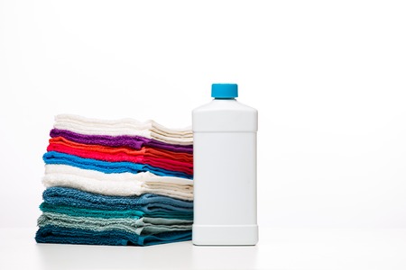 Photo of one bottle of detergent and multi-colored towels on clean white background