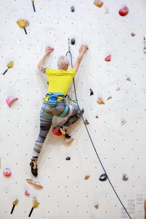 Photo from back of sports woman in yellow T-shirt scrambles up wall on workout in gymの写真素材