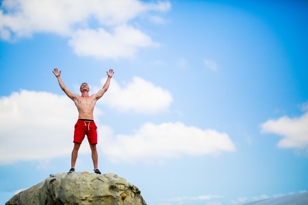 Photo of happy man climber on top of stone against blue skyの写真素材