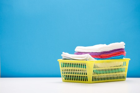 Photo of multi-colored terry towels in yellow basket on empty blue background.