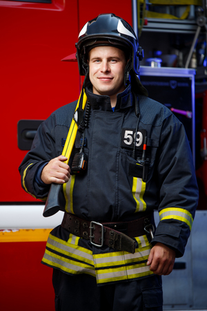 Photo of fireman wearing helmet with hammer against fire engine