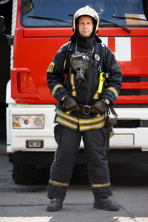 Photo in full growth of fireman on background of fire engine machine at stationの写真素材