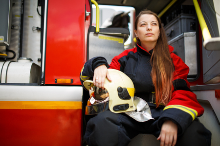 Photo of fire woman with long hair in overalls sits in fire truck