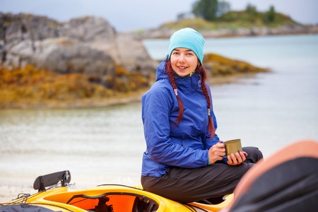 Photo of woman tourist with cup sitting on kayak on river