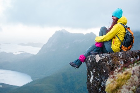Image of tourist woman with backpack sitting on top of mountain in background of picturesque landscapeの写真素材