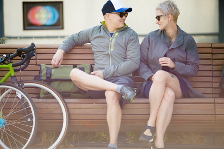 Image of man in sunglasses and women sitting on bench next to bicycleの写真素材