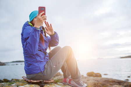 Woman sitting on stone with phone in hands on seashoreの写真素材
