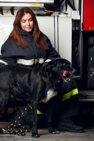 Portrait of female firefighter with black dog sitting on background of fire truckの写真素材