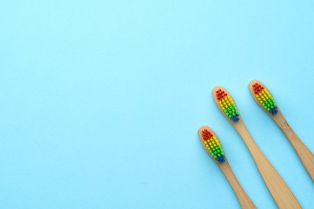 Photo of three wooden toothbrushes with rainbow-colored bristles.の写真素材