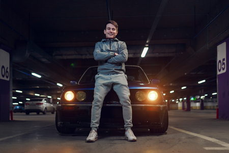 Photo of man with arms crossed standing on car in underground parking.の写真素材