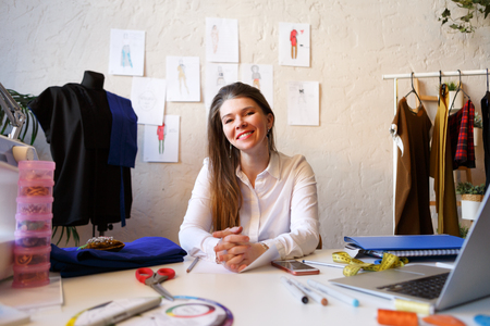 Photo of female dressmaker sitting at table with sewing machine and laptopの写真素材