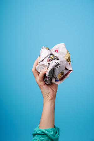 hand with crumpled newspaper on blue backgroundの写真素材