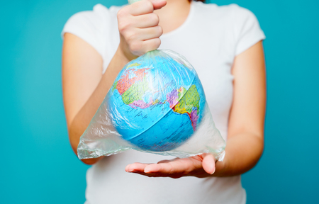 Woman holds in hands plastic bag with planet earth at blue background. The concept of plastic pollution.の写真素材