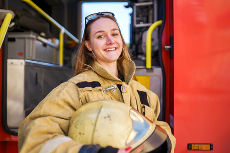 Photo of smiling woman firefighter with glasses on head standing next to fire truck at fire stationの写真素材