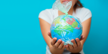 Woman holds in hands plastic bag with planet earth at blue background. The concept of plastic...