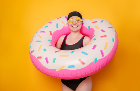 Picture of happy woman in swimming goggles, swimsuit with donut life buoy on empty orange backgroundの写真素材