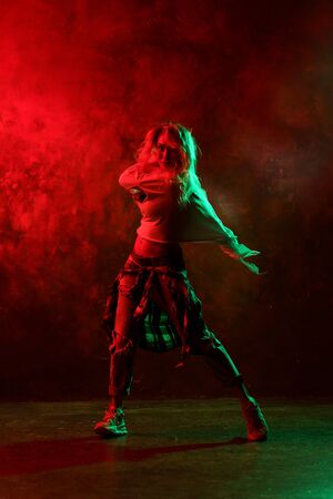 Photo of young woman in jeans dancing modern dances on red-green backgroundの写真素材