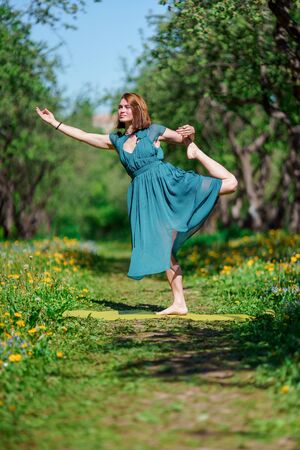 Photo of young woman in long green dress doing yoga in forestの写真素材