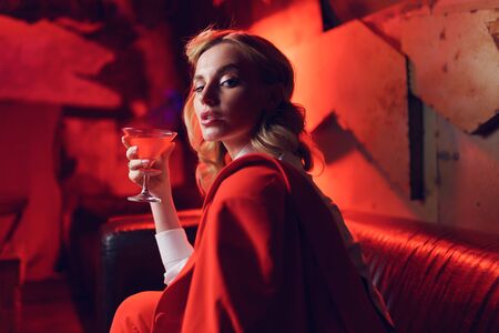 Photo of young blonde in red jacket with cocktail in her hand in nightclubの写真素材