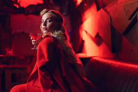 Image of young blonde woman in red jacket with cocktail in her hand in nightclubの写真素材