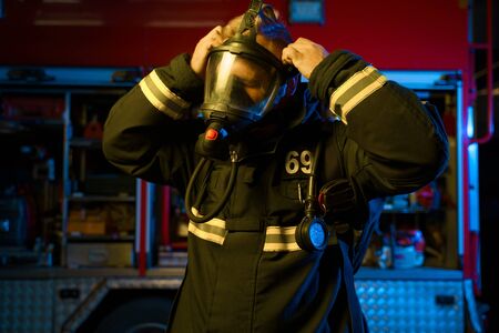 Photo of fireman putting on gas mask on background of fire engine at fire station. Neon effect