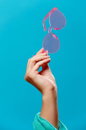 Photo of hand with pink sunglasses on empty blue backgroundの写真素材